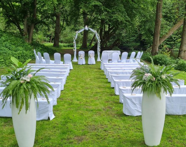 Grüne Wiese am Alsterlauf auf der weiß dekorierte Sitzbänke und Stühle für eine freie Trauung bereit stehen