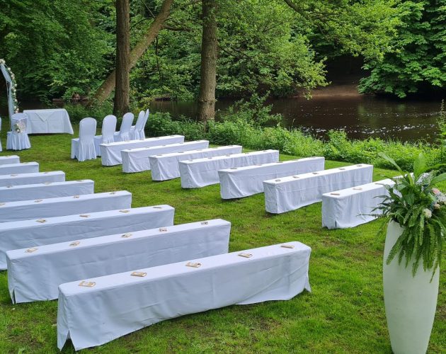 Wiese am Alsterlauf mit Bänken in weißen Hussen für eine Trauung im Rahmen einer Hochzeit im Alstertal