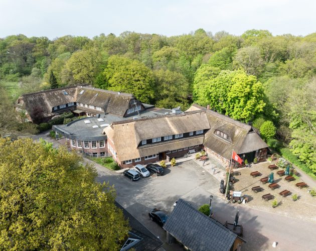 Luftbild auf dem das Gebäude des Hotels und Restaurants zu sehen ist, im Hintergrund die grünen Bäume des Alstertals