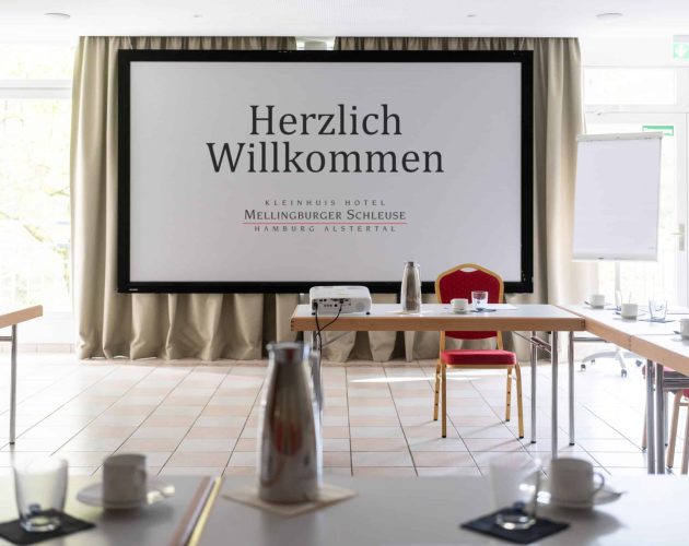 Tagungsraum Alster mit Tischen in U Form, einem Beamer und einer heruntergerollten Leinwand