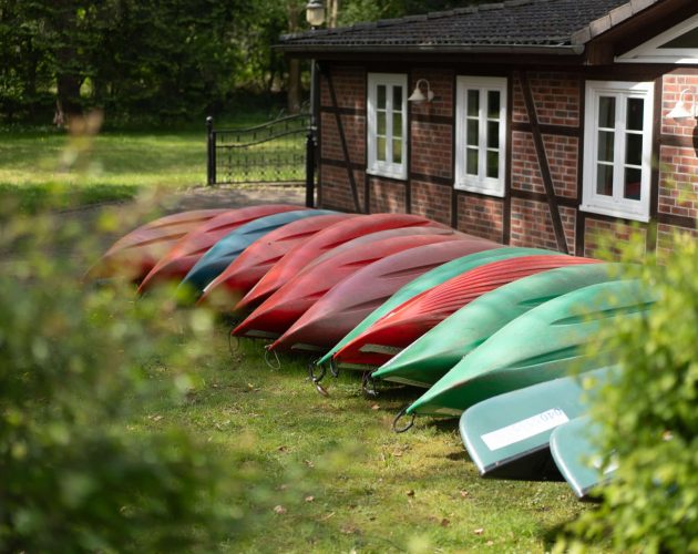 Auf dem Kopf liegende Kanus des ansässigen Kanuverleihs auf einer grünen Wiese