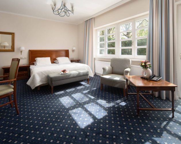 Hotelzimmer mit großzügiger Fenster Seite, blauem Teppichboden und Möbeln aus Holz