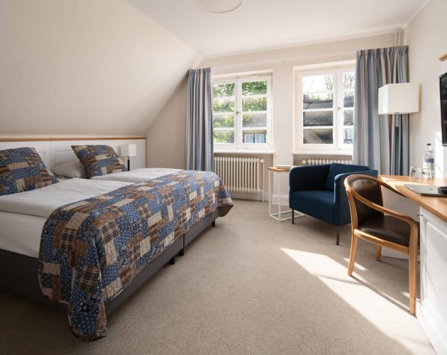 Hotelzimmer mit Bett, Schreibtisch und Sitzgelegenheit vor dem Fenster