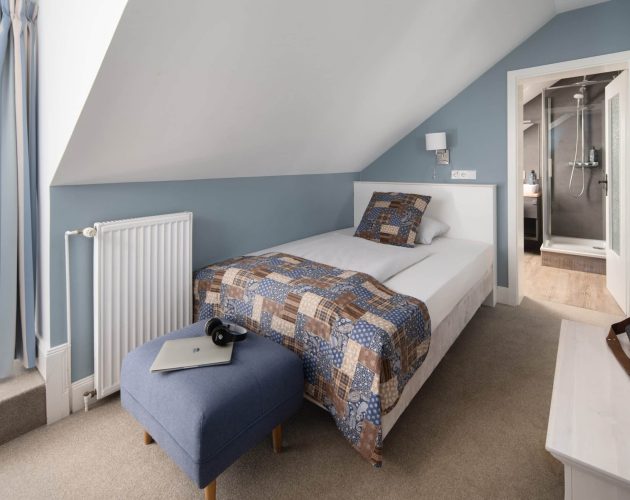 Hellblau gestrichenes Hotelzimmer mit einem französischen Bett unter einer Dachschräge