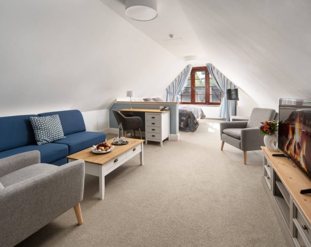 Großzügiges Hotelzimmer mit Sitzecke und Fernseher, im Hintergrund ist ein Bett zu sehen