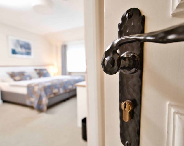 Geöffnete Zimmertür mit Blick auf das dahinterliegende Bett eines Hotelzimmers