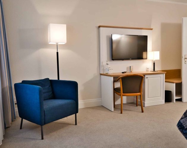 Schreibtisch mit Holzplatte und blauer Sessel in einem Hotelzimmer